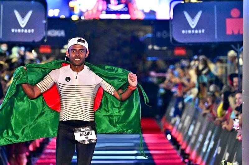 Mishu Biswas runs down the IRONMAN finish carpet holding the flag of Bangladesh behind him