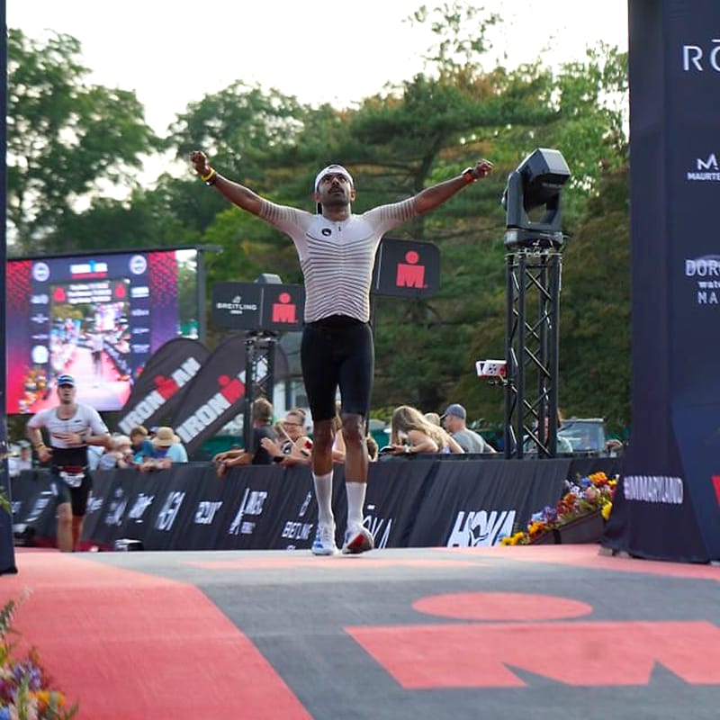 Mishu Biswas raises both arms as he crosses the IRONMAN Maryland 2026 finish line